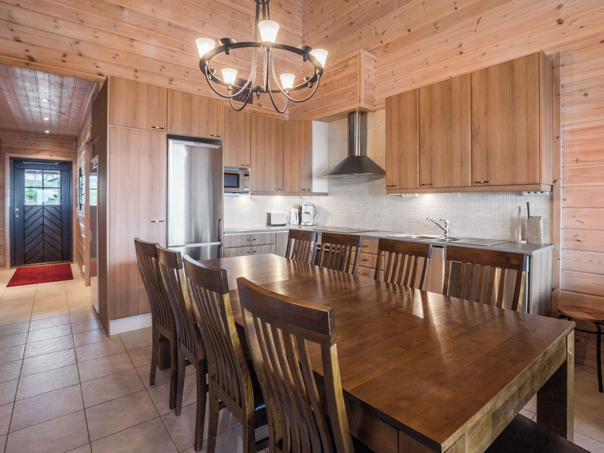 A modern kitchen with wooden cabinetry, a central island with chairs, stainless steel appliances, and a chandelier.