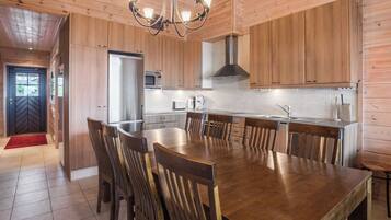 A modern kitchen with wooden cabinetry, a central island with chairs, stainless steel appliances, and a chandelier.