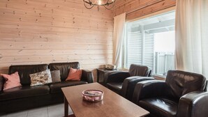 A cozy living room with a wooden ceiling, a black leather sofa, a wooden coffee table, and leather armchairs.