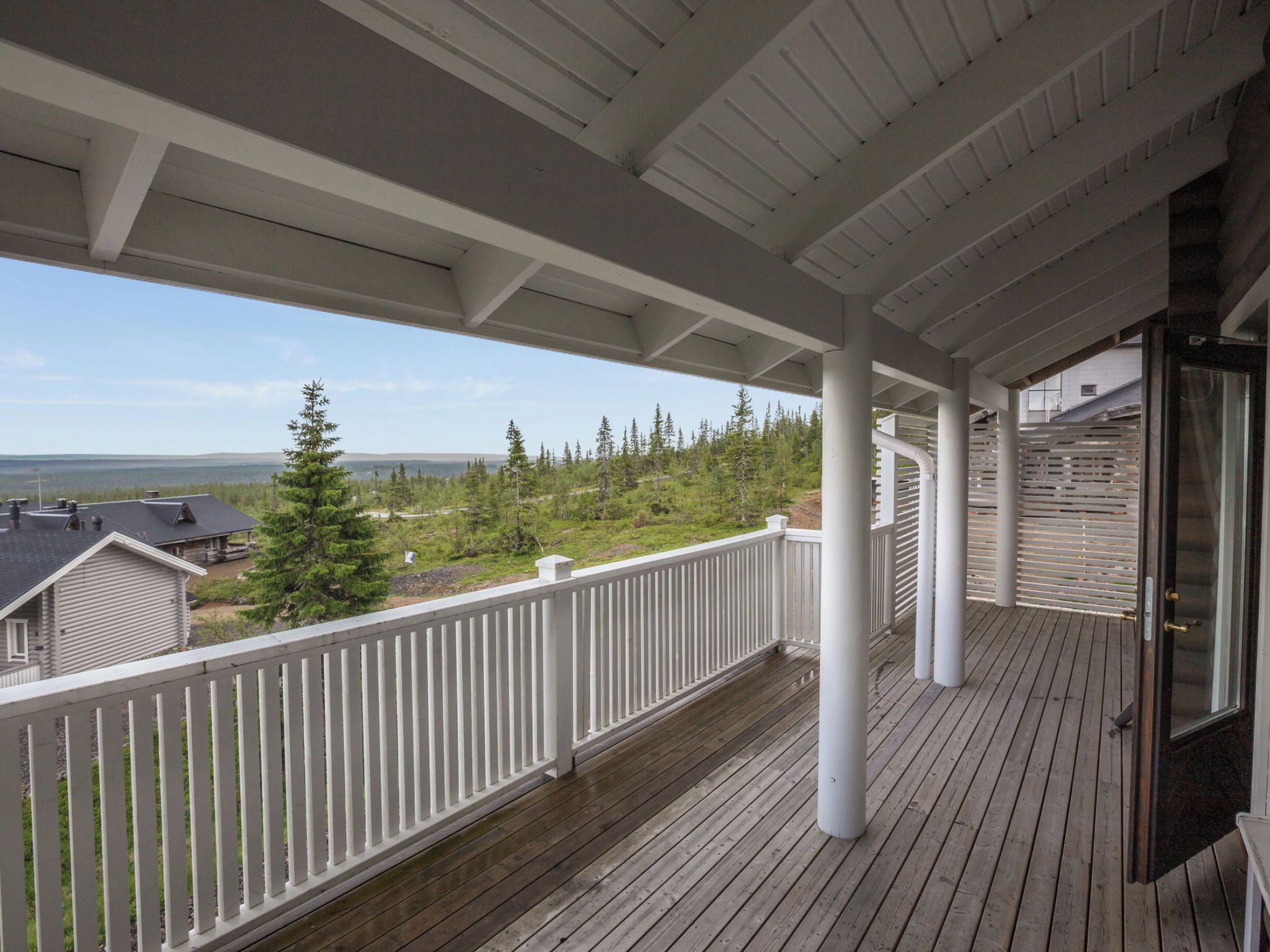 A wooden deck with a white railing, overlooking a forested area and a body of water.