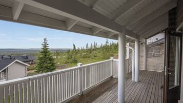 A wooden deck with a white railing, overlooking a forested area and a body of water.