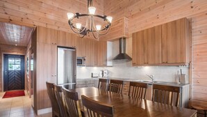 A modern kitchen with wooden cabinetry, a stainless steel refrigerator, a microwave, and a gas stove. There is a large wooden dining table with chairs.