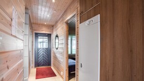 A narrow hallway with wooden walls and a tiled floor, leading to a room with a bed and a white refrigerator.