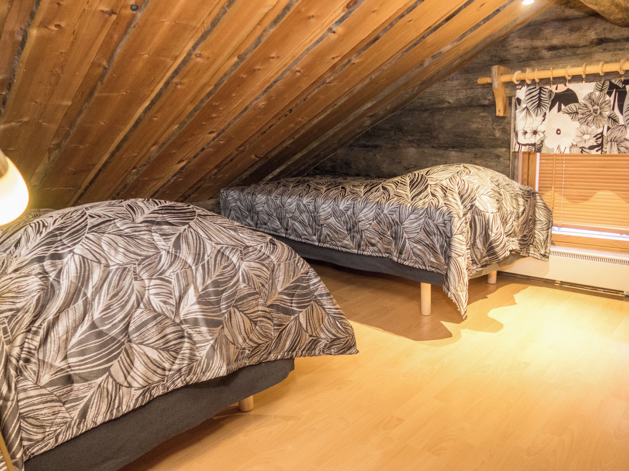 A room with two beds, wooden flooring, and a sloped ceiling.