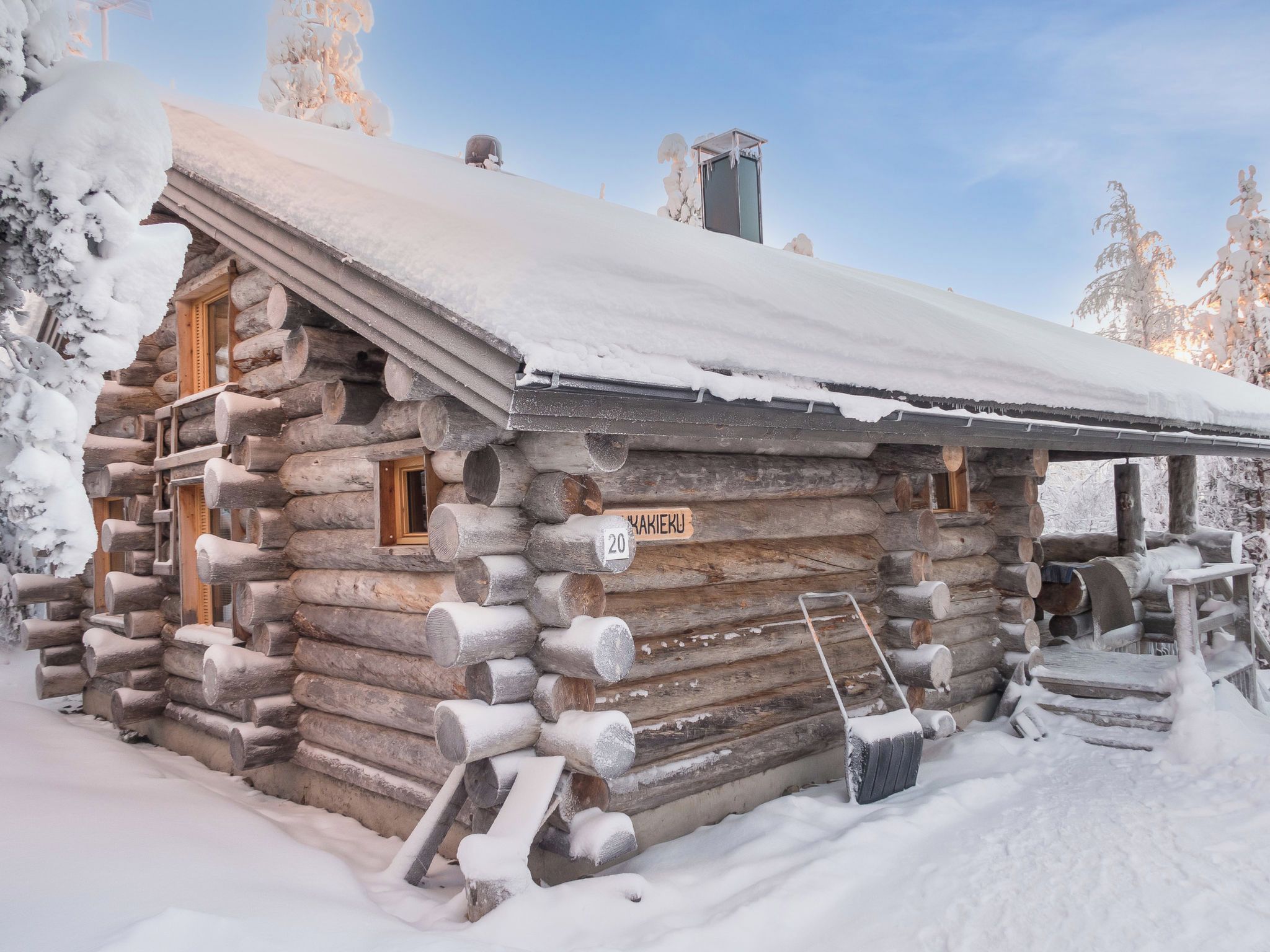 Una cabaña de troncos con techo nevado, paredes de madera y una chimenea.