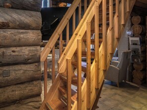 A wooden staircase in a log cabin interior with a fireplace and a bear statue.