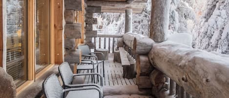Una baita di legno con veranda, zona salotto e vista su alberi innevati.