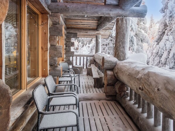 A log cabin with a wooden deck, seating area, and a view of snow-covered trees.