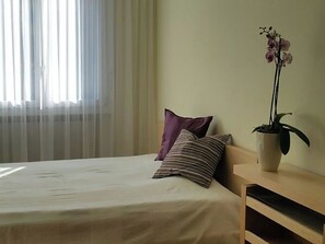 A hotel room with a bed, a nightstand, a potted orchid, and sheer curtains.