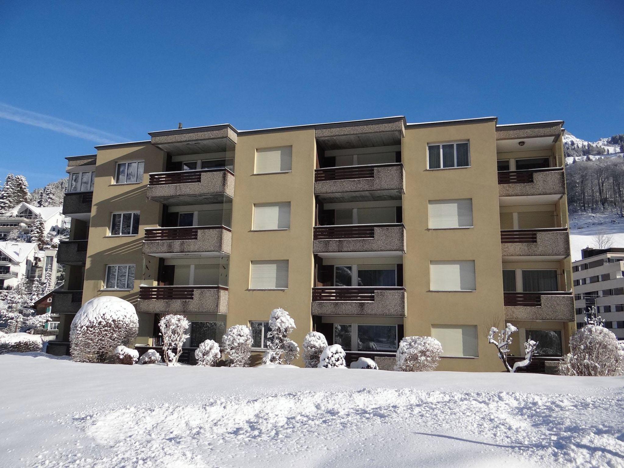A multi-story hotel with balconies, a snow-covered landscape, and a mountain in the background.