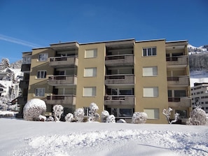 A multi-story hotel with balconies, a snow-covered landscape, and a mountain in the background.