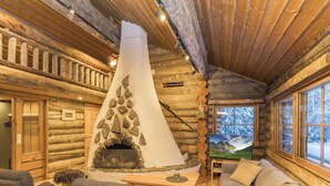 A log cabin interior with a stone fireplace, wooden furniture, and a TV. - Rukasaukko by Interhome (Kuusamo)
