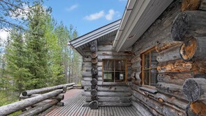 A log cabin with a wooden deck, a window with curtains, and a view of the surrounding forest. - Rukasaukko by Interhome (Kuusamo)
