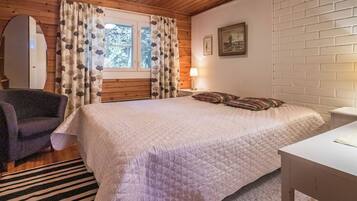 A bedroom with a bed, a chair, a bedside table, a lamp, and a window with curtains.