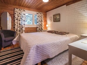 Een slaapkamer met een bed, een stoel, een nachtkastje, een lamp en een raam met gordijnen.