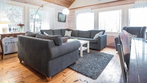 Una sala de estar acogedora con techo de madera, un sofá seccional, una mesa de comedor y ventanas grandes.