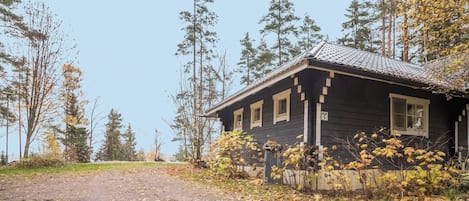 A rustic cabin with a dirt path leading to it, surrounded by trees and autumn foliage.