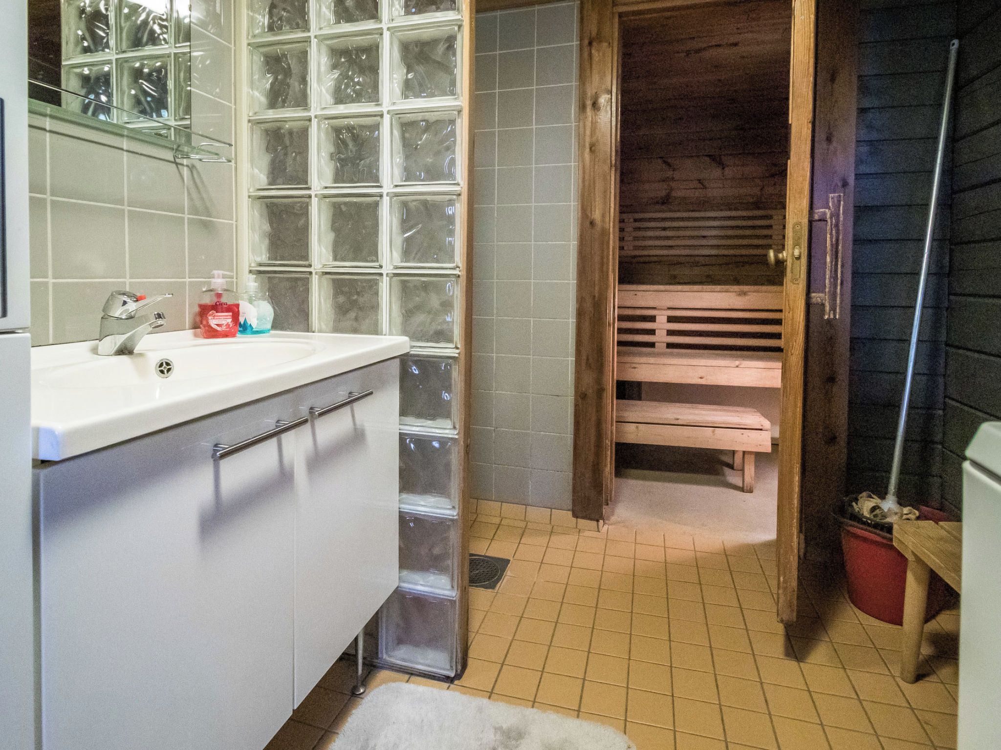 A bathroom with a white sink, a mirror, a window with frosted glass, and a wooden bench.