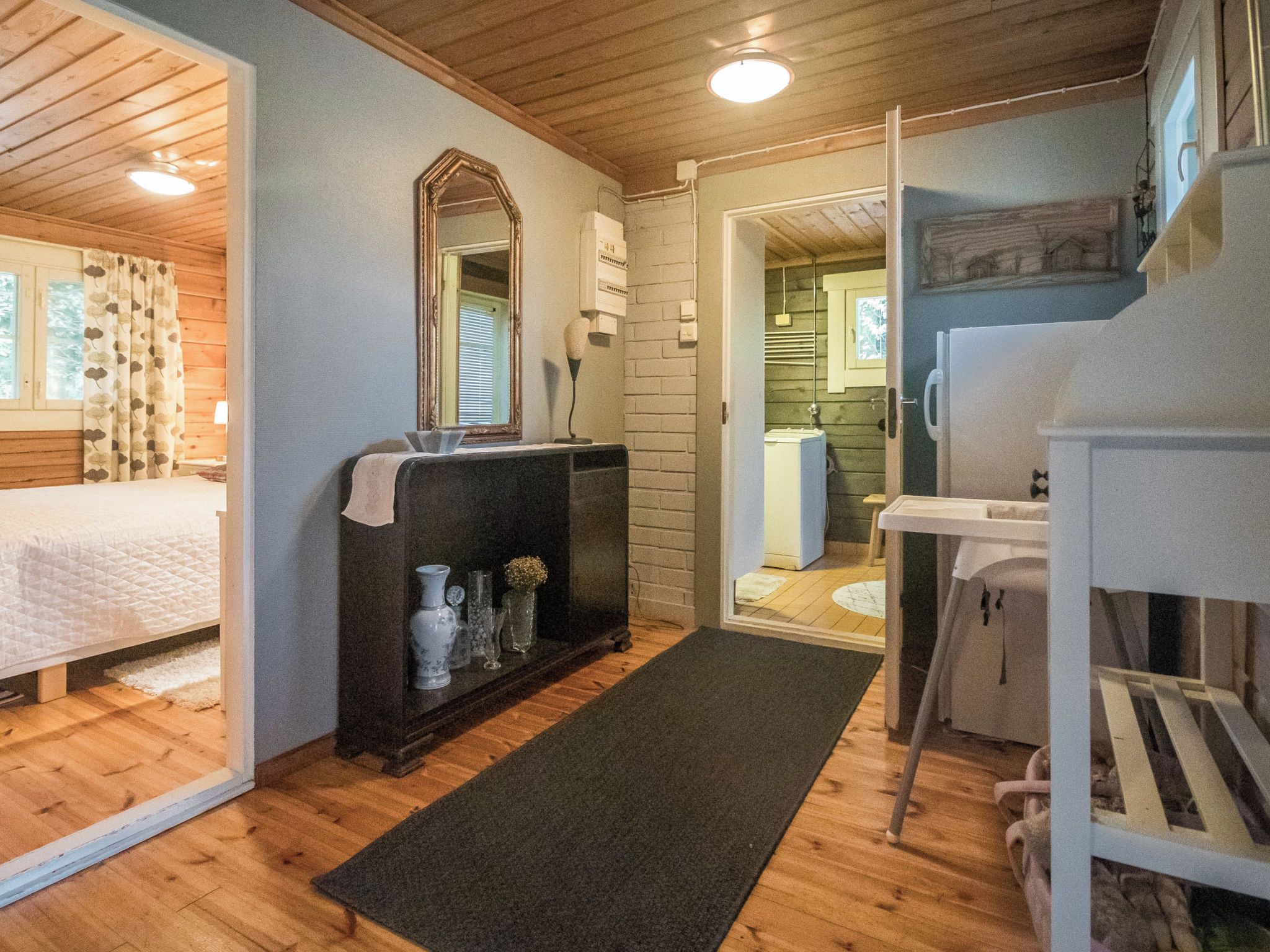 A cozy room with a bed, a dresser with decorative items, a mirror, and a door leading to another room.