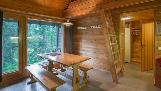 Een houten blokhutinterieur met een houten tafel en banken, een ladder en een deur die leidt naar een kast.