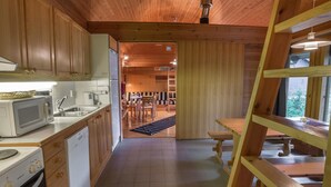 Een keuken met houten kastjes, een magnetron, een fornuis en een spoelbak. Er is een eethoek met een tafel en stoelen.