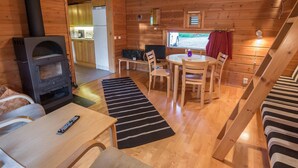 Een gezellig interieur van een chalet met een houtkachel, een eethoek en een trap.