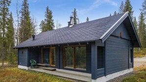 Een chalet met een donkerblauwe buitenkant, grote ramen en een overdekte veranda met een bankje.
