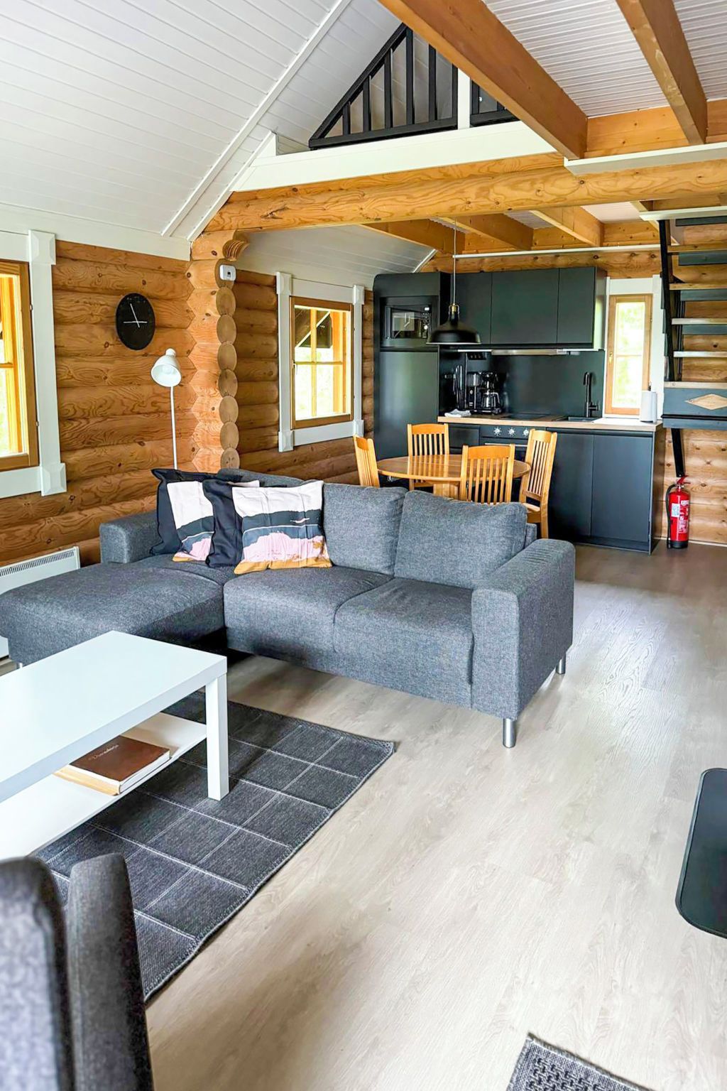 En modern inredning i en timmerstuga med en grå hörnsoffa, ett matbord och ett köksområde.