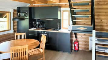 A compact kitchen with a dining table and chairs, a coffee machine, and a fire extinguisher.