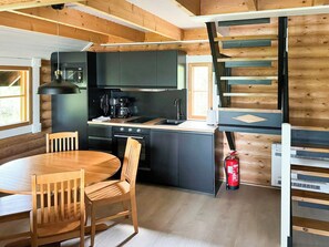 A compact kitchen with a dining table and chairs, a coffee machine, and a fire extinguisher.