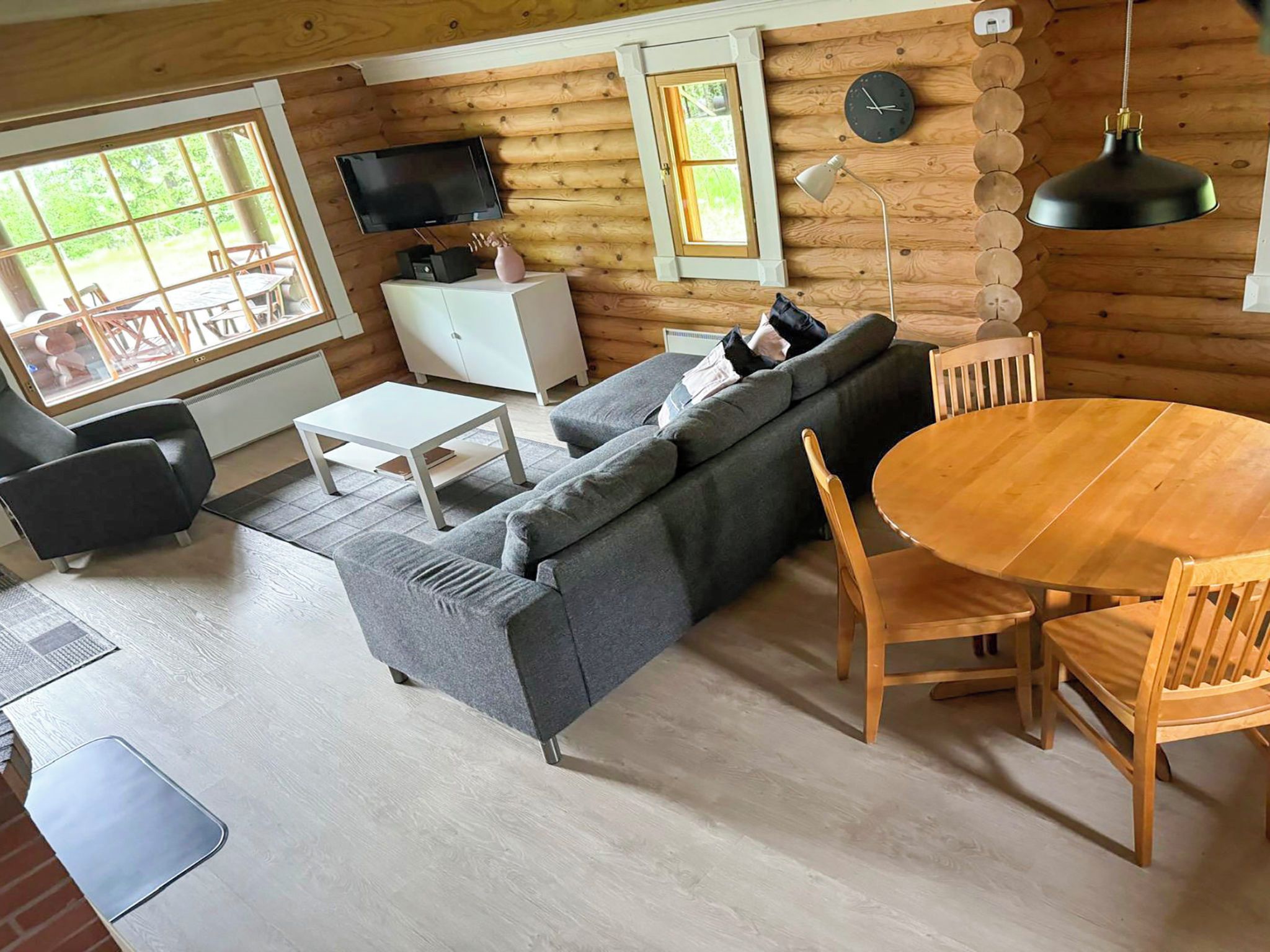 Hirsihirrestä rakennetun mökin sisustus: siellä on sohva, ruokapöytä, tuoleja, televisio ja seinällä oleva kello.