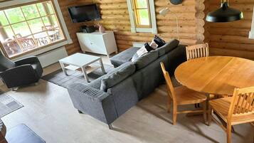 Hirsihirrestä rakennetun mökin sisustus: siellä on sohva, ruokapöytä, tuoleja, televisio ja seinällä oleva kello.