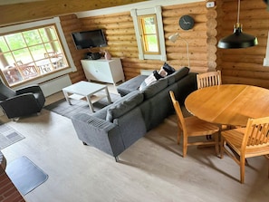 A log cabin interior with a sofa, dining table, chairs, a TV, and a clock on the wall. - Metsä-pihlaja by Interhome (Kinnula)