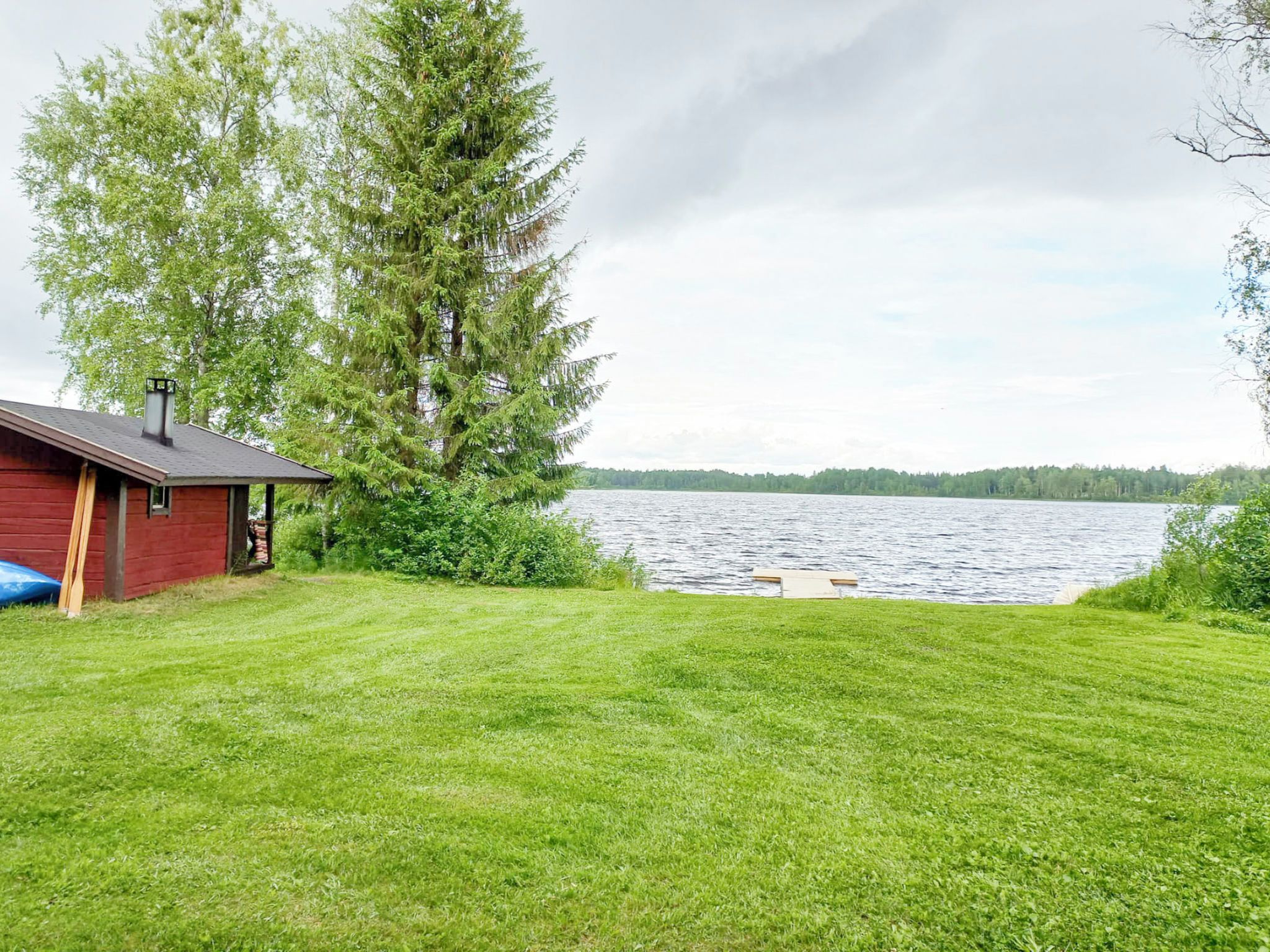 A grassy yard with a red building and a large tree.