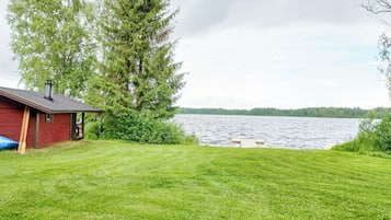 A grassy yard with a red building and a large tree.