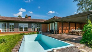 Uma piscina com escada, cercada por uma área de brita e um gramado.