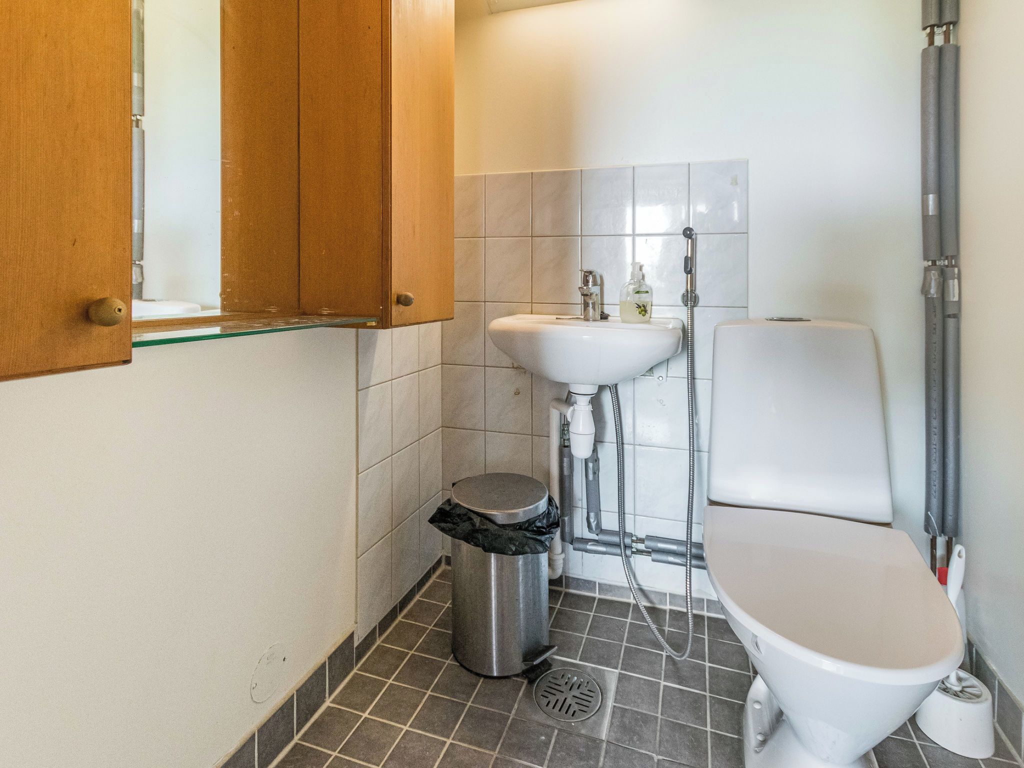 A small bathroom with a toilet, sink, and shower. There is a trash can and a window above the sink.