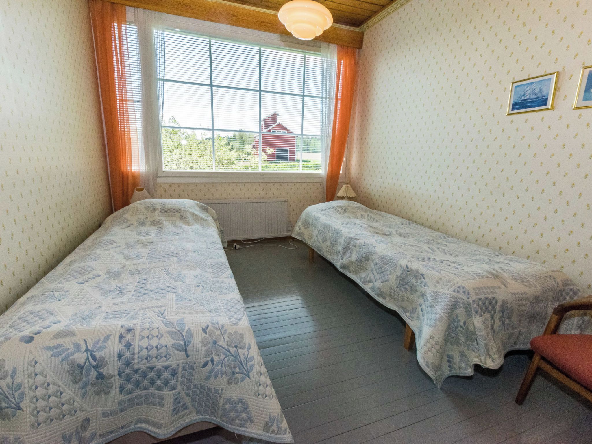 A room with two single beds, a window with curtains, a radiator, and a small chair.