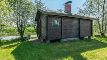 Puuinen mökki, jossa on savupiippu, pieni ikkuna ja ruohikkoon kasvanut piha.