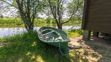 A green boat tied to a tree by a body of water, with a wooden structure in the background.