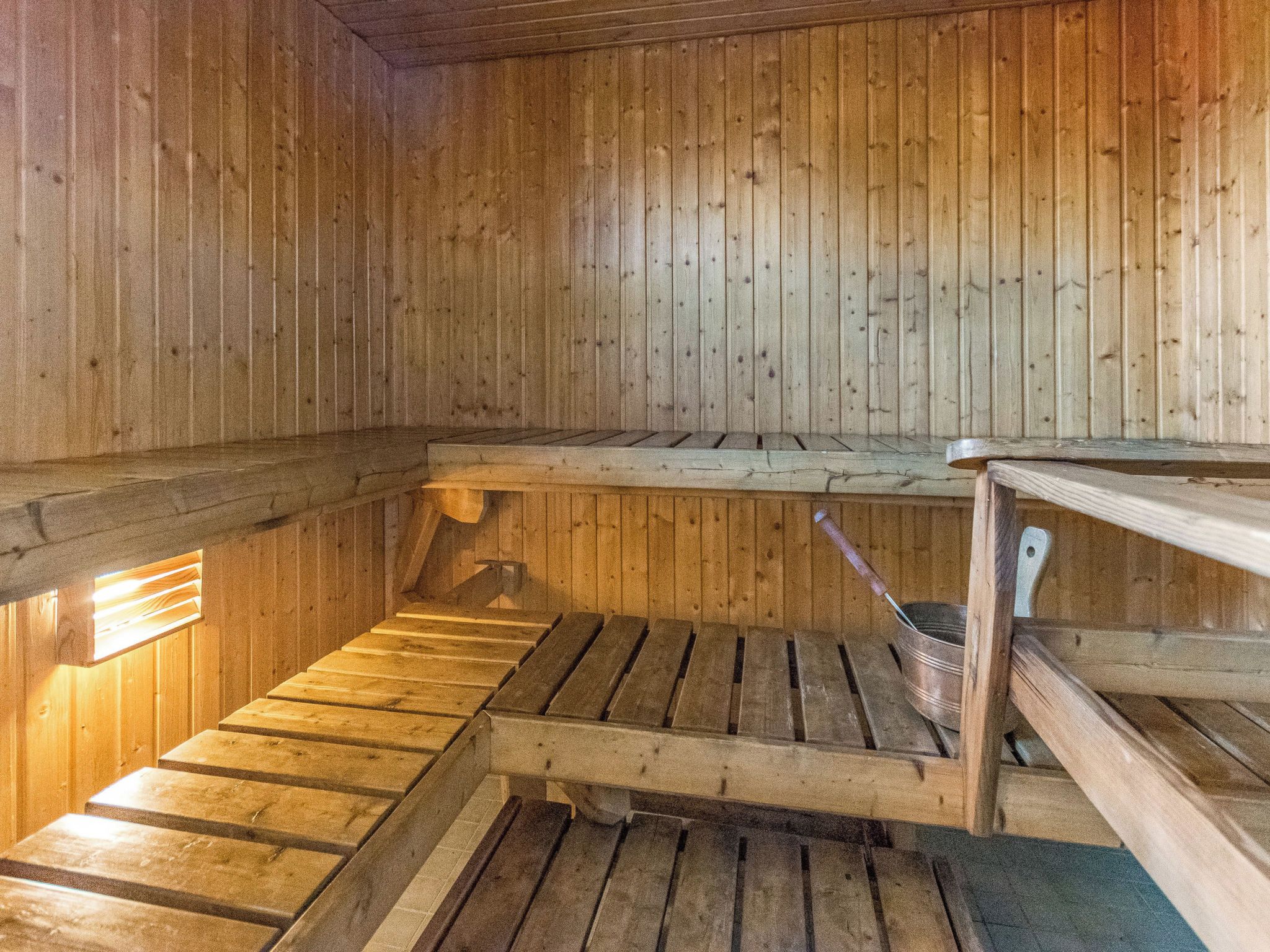 Un sauna avec des bancs en bois et un seau en métal.