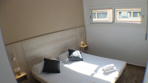 A neatly made bed with pillows, a bedside table with a lamp, and a window with blinds. - Rescator Resort 224 - One Bedroom Resort, Sleeps 4 (Roses)