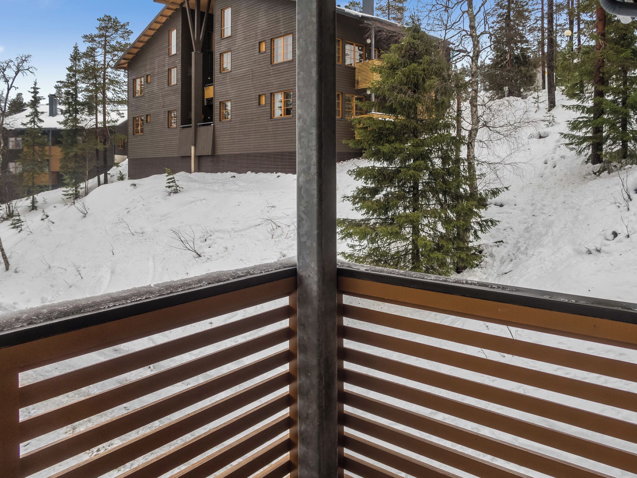 Un balcón de madera con vistas a un edificio y tierra cubierta de nieve.