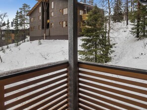 Un balcón de madera con vistas a un edificio y tierra cubierta de nieve.