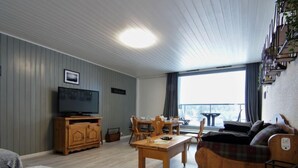 Tunnelmallinen olohuone, jossa on televisio, puuhuonekalut ja suuri ikkuna, josta avautuu kaunis näkymä.