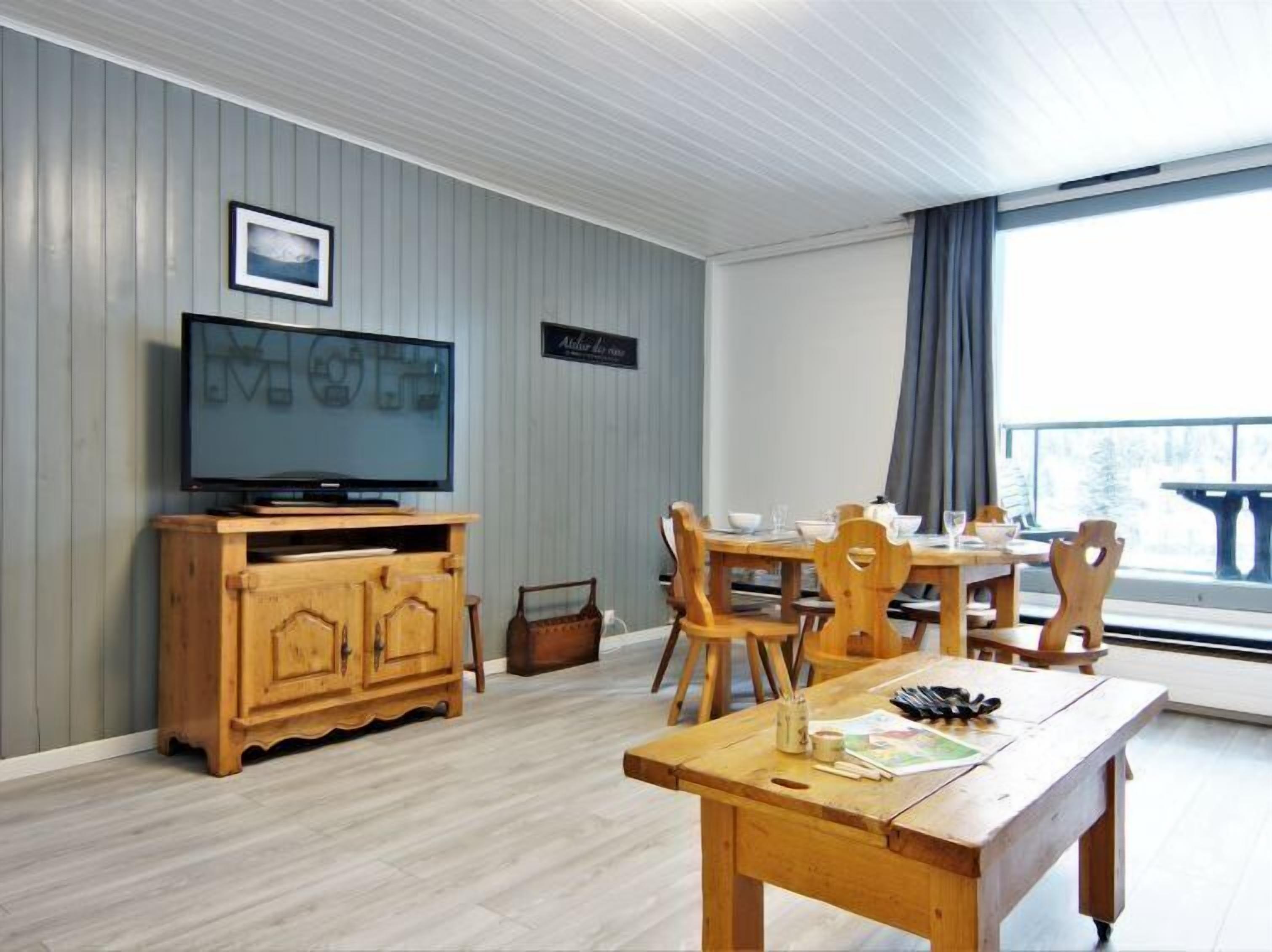 A living room with a television, wooden furniture, a dining table, and a view of the outdoors.