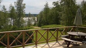 Une terrasse en bois avec une table de pique-nique et un parasol, entourée d’une balustrade en bois et de verdure.