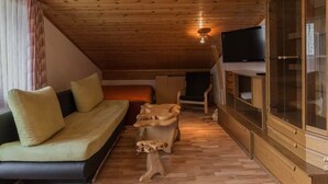 Habitació acollidora amb sostre de fusta, un sofà amb coixins, una taula petita, un armari i una televisió.