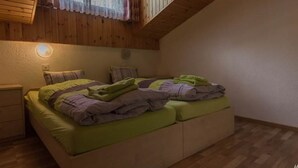 Un dormitori amb sostre de fusta, un llit amb roba de llit verd i morada, una tauleta de nit i una làmpada penjada a la paret.