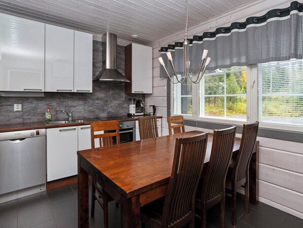 A modern kitchen with white cabinets, a Bosch dishwasher, a stainless steel range hood, and a dining area with a wooden table and chairs.